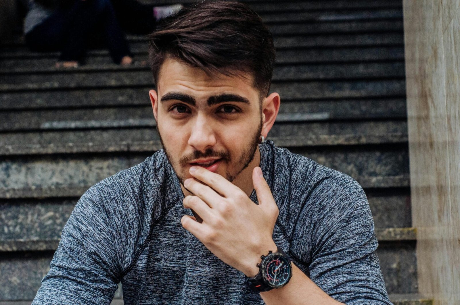 A casually dressed young man posing thoughtfully on outdoor steps, exuding style and confidence.